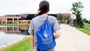 Prospective girl wearing a blue Cedarville drawstring bag on her back walking around the lake.