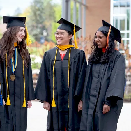 Three college students smiling in graduation regalia.